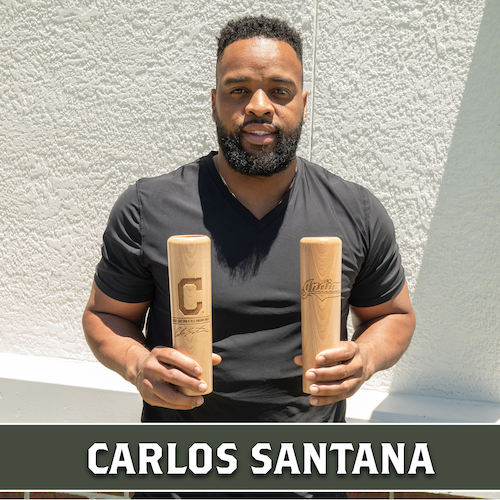 Carlos Santana holding two wooden Dugout Mugs baseball bat mugs with Cleveland team logos, with his name displayed in a banner at the bottom.
